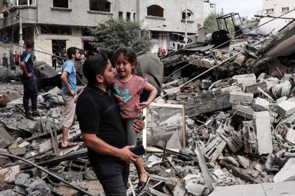 A man carries a crying child as he walks in front of a building destroyed in an Israeli air strike in Gaza City on October 7, 2023.