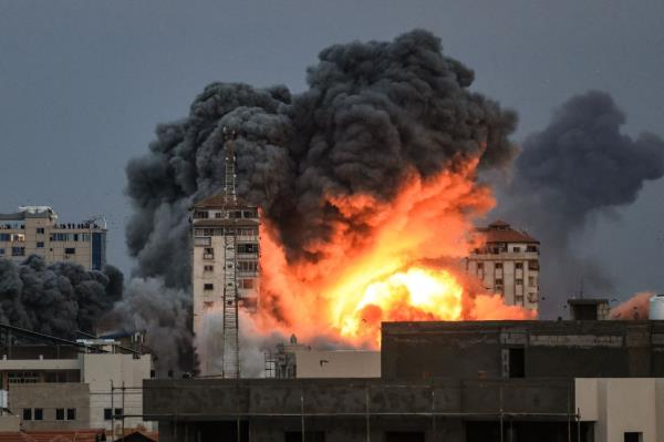 People standing on a rooftop watch as a ball of fire and smoke rises above a building in Gaza City on October 7, 2023 during an Israeli air strike.