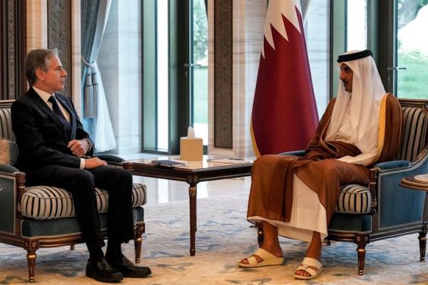 A man in a suit speaks to another man in traditional Gulf Arab dress.