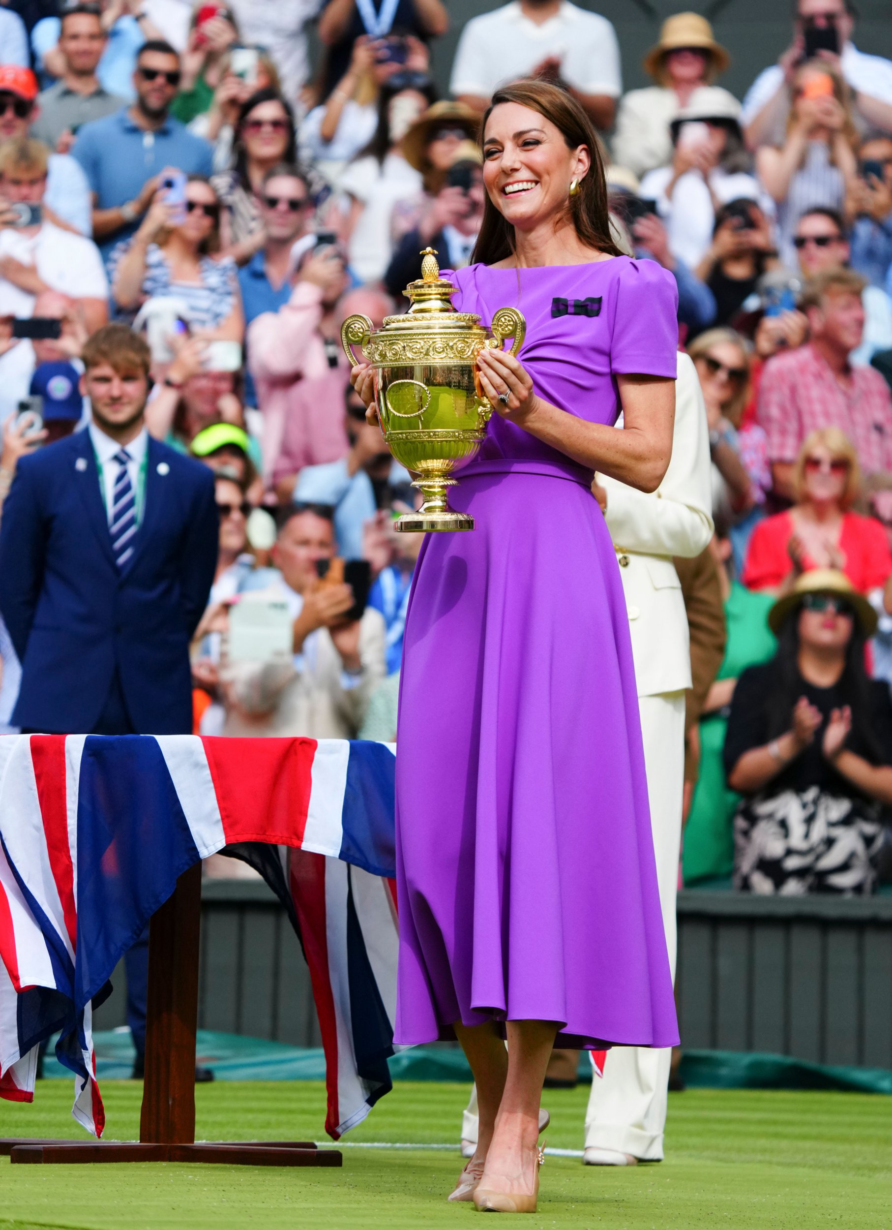 Kate Middleton holding a trophy at the Wimbledon men's singles in a purple dress. 