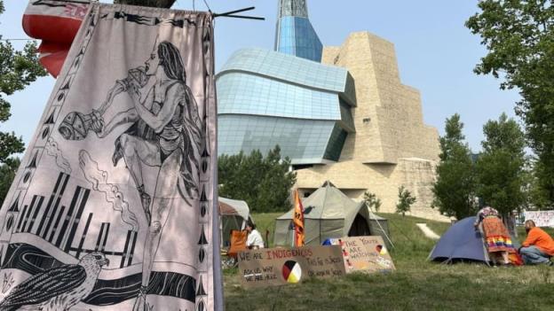 Signs and tents outside a glass and stone building