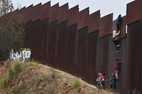 A group of adult and child migrants climbing the border wall between Tijuana and San Diego, seeking asylum in the United States