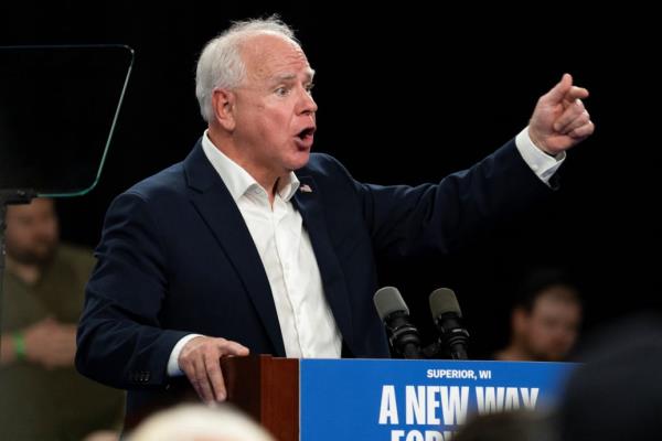 Tim Walz speaks behind a podium at a campaign rally.